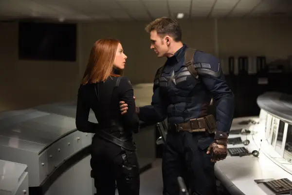 Chris Evans in Captain America outfit holding the arm of Scarlett Johansson in Black Widow suit. They are looking into each other