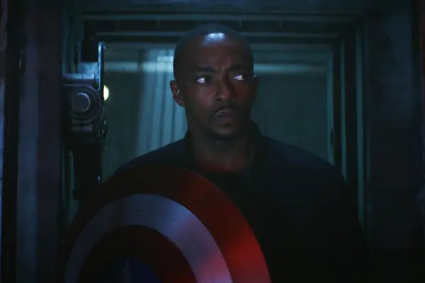 Anthony Mackie plays Sam Wilson in Captain America: Brave New World, wearing civilian clothes but holding his classic shield in a dark room