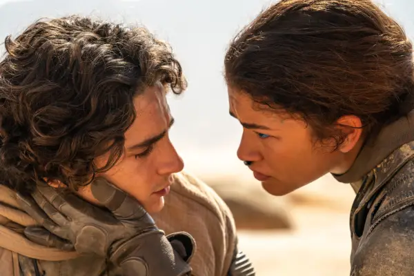 Timothee Chalamet as Paul Atreides has his face held by Zendaya as Chani on the sand dunes of Dune: Part Two.