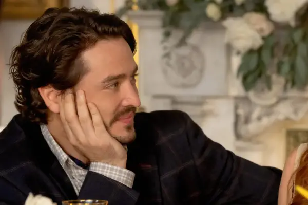 Alexander Vlahos plays Paul Kennedy in Irish Wish. He is looking to the side with his hand resting on his cheek