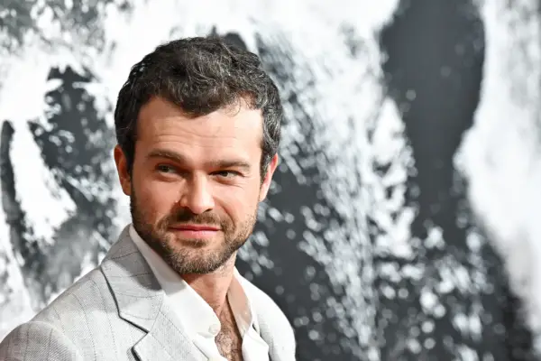 Alden Ehrenreich in a grey suit jacket and white shirt