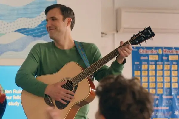 Dan Bulla as Cantor Jerry in You Are So Not Invited to My Bat Mitzvah playing an acoustic guitar