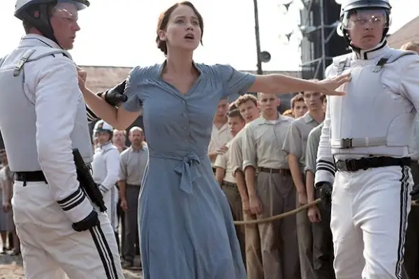 Jennifer Lawrence wearing a blue dress in The Hunger Games, pushing two guards