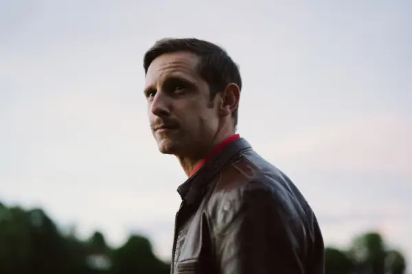 Andrew Scott as Adam sits in his apartment with the skyline in the background at night in All of Us Strangers