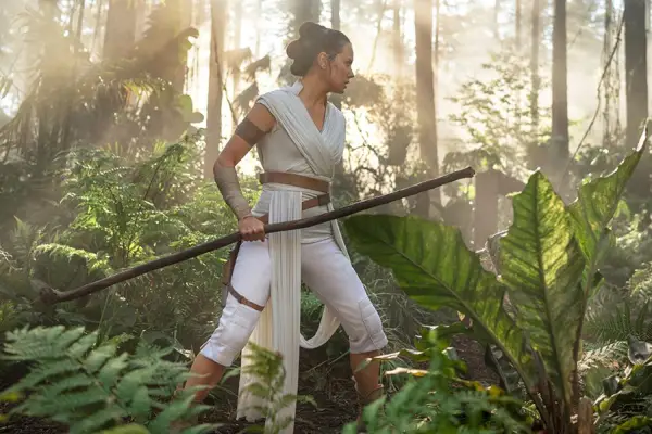 Daisy Ridley as Rey in Star Wars: The Rise of Skywalker walking through the woods with a staff