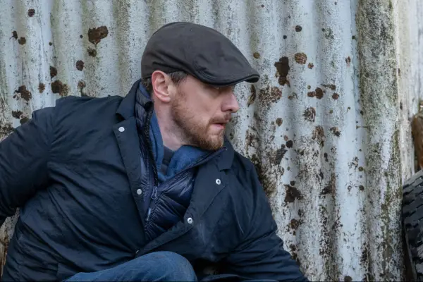 James McAvoy as Edmond Murray crouching by a rusty wall in a flat cap
