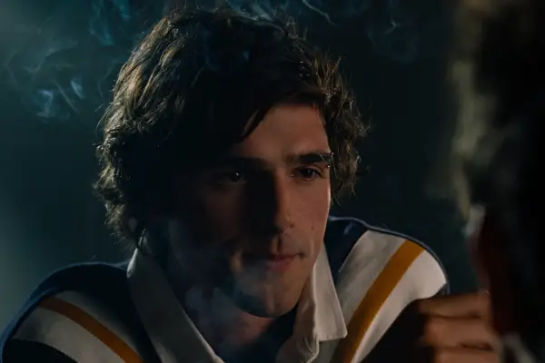 Jacob Elordi smoking in Saltburn wearing a striped shirt, smirking