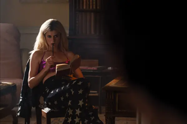 Alison Oliver as Venetia Catton in Saltburn sitting with a book in one hand and a pen in the other