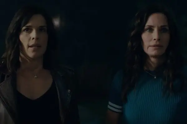 Neve Campbell and Courteney Cox in Scream (2022) standing and looking shocked