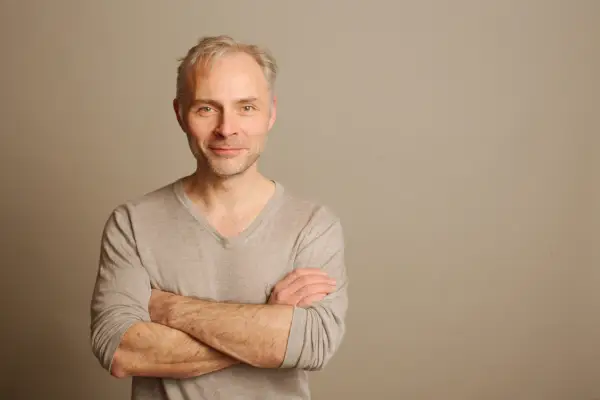 Mark Bonnar wearing a brown jumper with his arms crossed