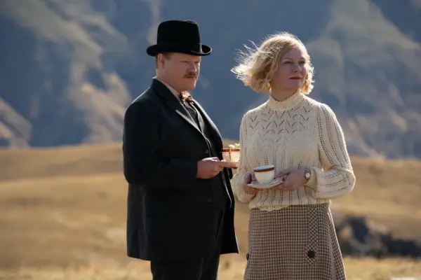 JESSE PLEMONS as GEORGE BURBANK, KIRSTEN DUNST as ROSE GORDON in THE POWER OF THE DOG standing together, holding tea cups