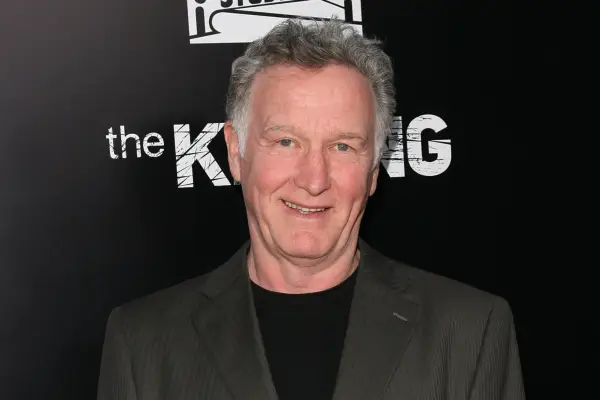 Tom Butler wearing a dark jacket and T-shirt and sat against a dark backdrop, with the word 