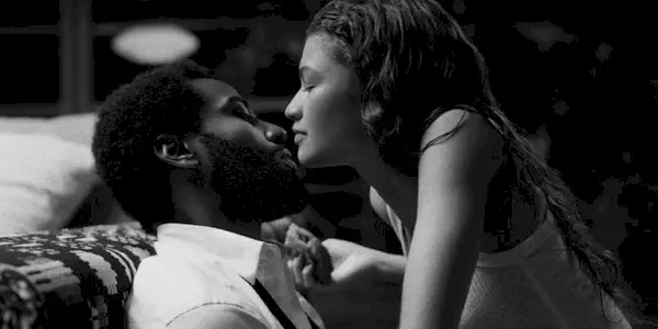 Malcolm sits back on a couch as Marie leans in to kiss him. 