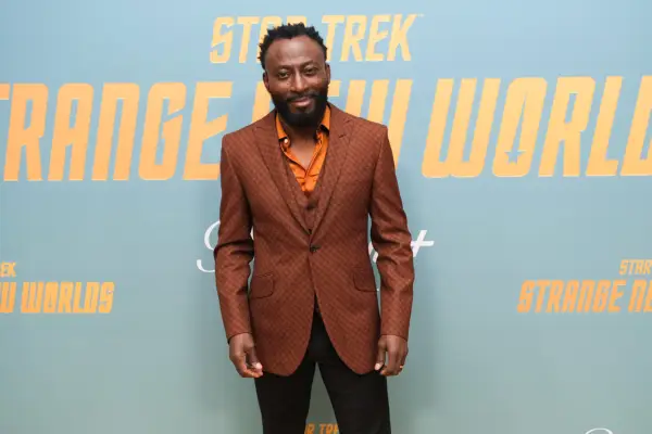 Babs Olusanmokun in a brown suit jacket and orange shirt