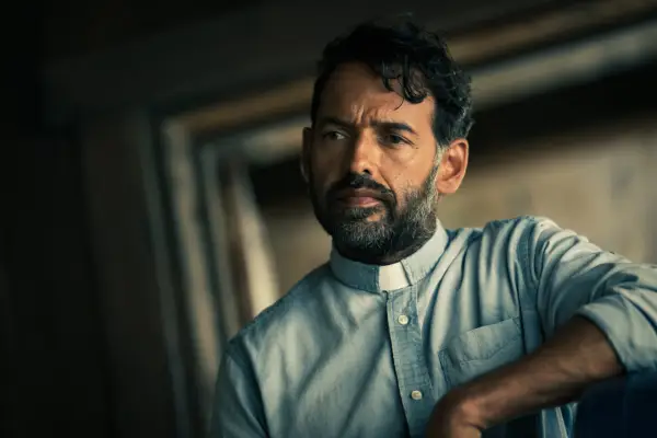 Shaun Majumder as Father Khatri in From, wearing a blue shirt and clerical collar