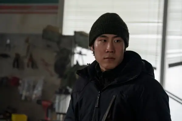 Young Mazino in The Last of Us season 2, wearing a hat and coat and looking worried.