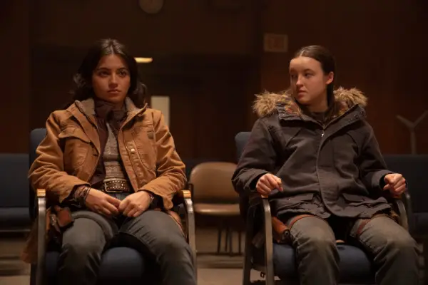 Isabela Merced as Dina and Bella Ramsey as Ellie in The Last of Us season 2 sitting down and looking stressed.