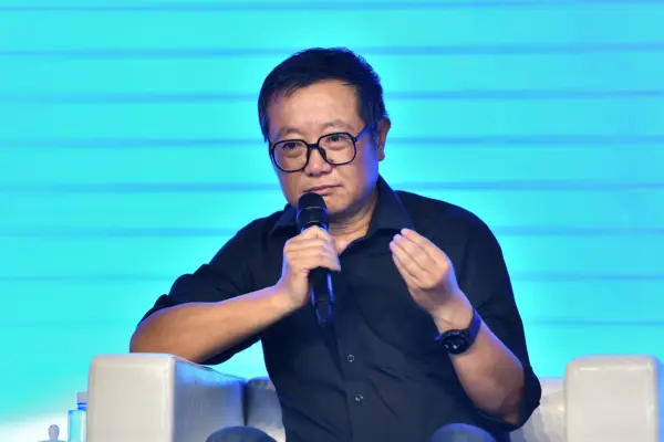 Liu Cixin speaks at a panel, holding a microphone and stood in front of a blue background