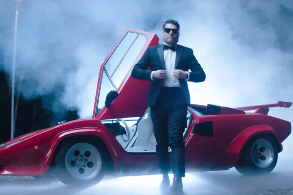 Adam Pally as Wade Whipple in Knuckles, wearing a tuxedo in front of a red sports car