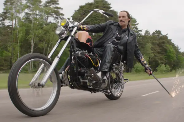 Julian Barratt as Jack Sinclair in Knuckles riding a motorcycle dragging a blade along the ground