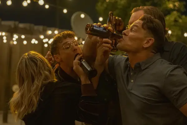 The main cast of Peacemaker in a scene from season 2. Harcourt, Adrian, Adebayo, Economos and Chris are having a party, drinking together from glass beer bottles