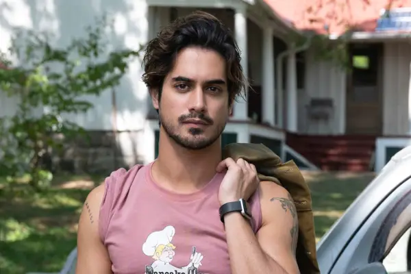 Jack (Avan Jogia) wearing a pink vest, holding a jacket over his shoulder