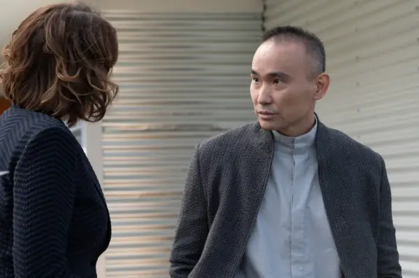James Hiroyuki Liao as Darros in Orphan Black: Echoes wearing a grey shirt and cardigan, talking to Hawes