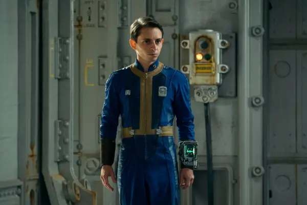 Moisés Arias as Norm in Fallout in blue and yellow overalls and a Pip Boy on his arm