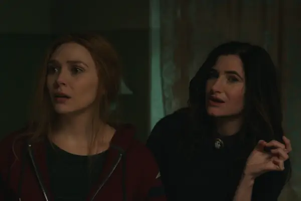 Elizabeth Olsen as Wanda Maximoff and Kathryn Hahn as Agatha Harkness in WandaVision standing next to each other looking concerned