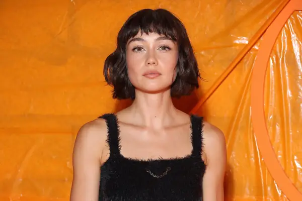 Sydney Chandler against an orange backdrop looking at the camera