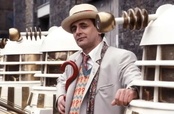 Doctor Who - Sylvester McCoy wearing a grey suit and beige hat, holding a staff