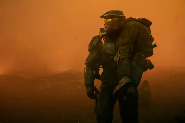 Pablo Schrieber as Master Chief in Halo season 2, holding a person over his shoulder and surrounded by orange light