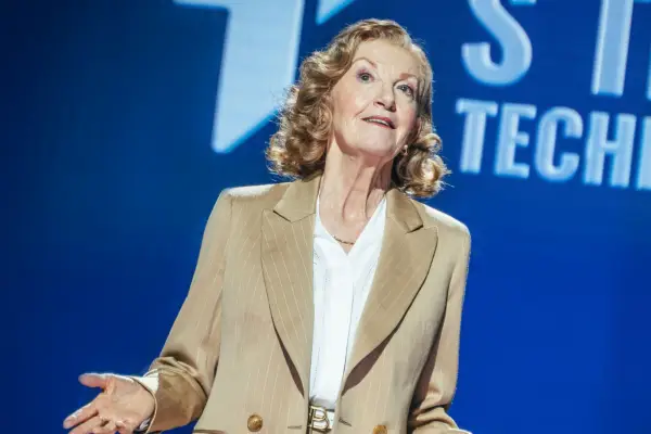Susan Twist wearing a white blouse and brown suit jacket, looking up.