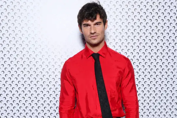 Paul Forman posing for a photo. He is wearing a bright red shirt and black tie as she looks ahead.