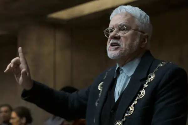 Tim Robbins, with a mayoral chain and around his neck, making a speech in Silo season 2