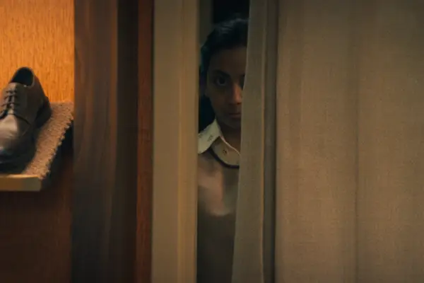 Anjana Vasan peering through a gap in a door