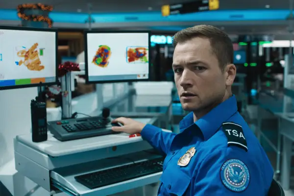 Taron Egerton stars in Carry-On in a TSA uniform using a computer
