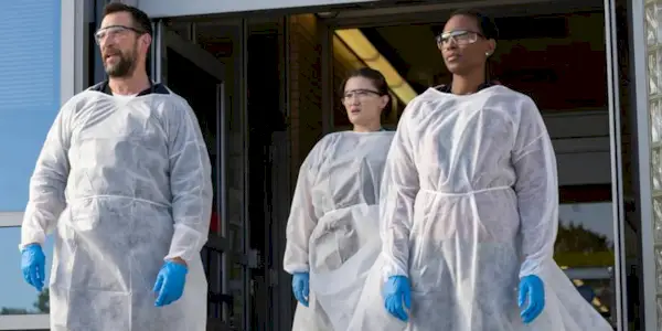Noah Wyle, Isa Briones, and Tracy Ifeachor stand in white protective gear, gloves, and goggles in 