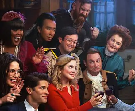 The ghosts surrounding Sam (Rose McIver) while drinking wine with her husband Jay (Utkarsh Ambudkar) in a still for Ghosts Season 4.