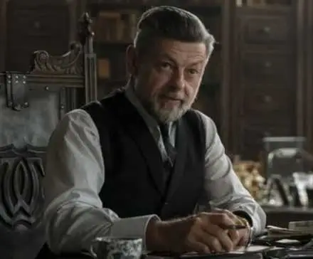 Andy Serkis as Alfred sitting at a table in a library or study room inside Wayne Manor in The Batman.
