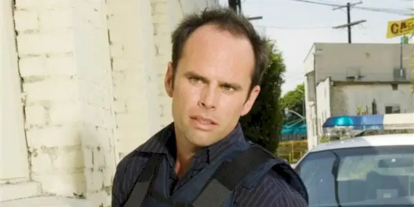 Walton Goggins as Shane looking to the side, wearing a bullet-proof vest with a cop car behind in The Shield.