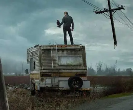 Alexander Skarsgard as Randall Flagg standing on top of a trailer holding a crow on the poster for The Stand miniseries