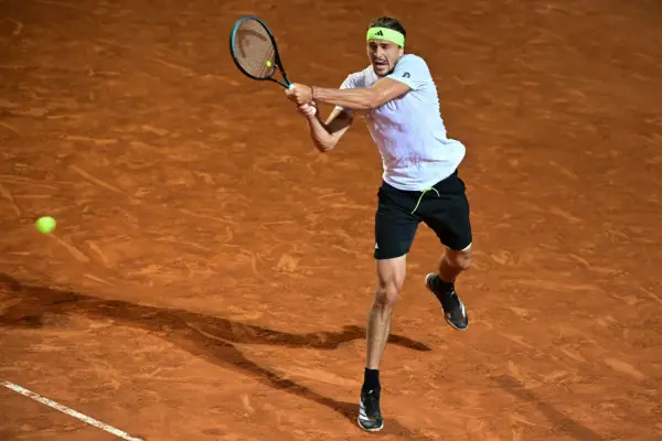 Alexander Zverev hits a backhand on clay court in a fluorescent yellow headband, white t-shirt, and black shorts