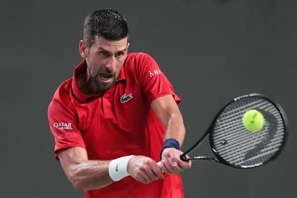 Novak Djokovic, in red Le Coq Sportif tennis shirt, hits a backhand.
