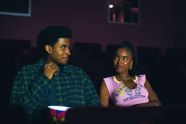 Michael Cooper Jr. as Justin Edwards and Lovie Simone as Keisha Clark, sat next to each other at the cinema, looking at one another and smiling
