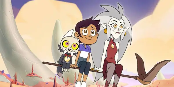 King, a dog like creature with horns, sits next to Dominican American teen, Luz, the human and Eda the witch all sitting on top of an owl staff that floats above the city. 