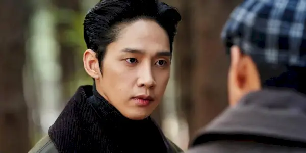 Park Sung-hoon looking at a man with a gingham hat in a still from the show 