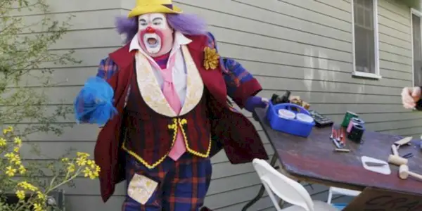 Actor Eric Stonestreet playing Cameron Tucker, dressed as the clown Fizbo, running away in Modern Family.
