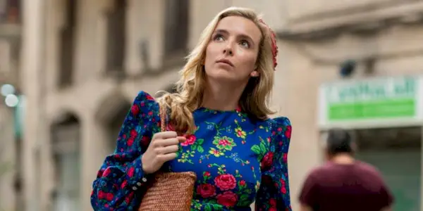 Jodie Comer as Villanelle in Killing Eve walking around holding a purse in a floral dress, looking up.