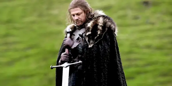Eddard Stark standing in an open field holding his sword in Game of Thrones